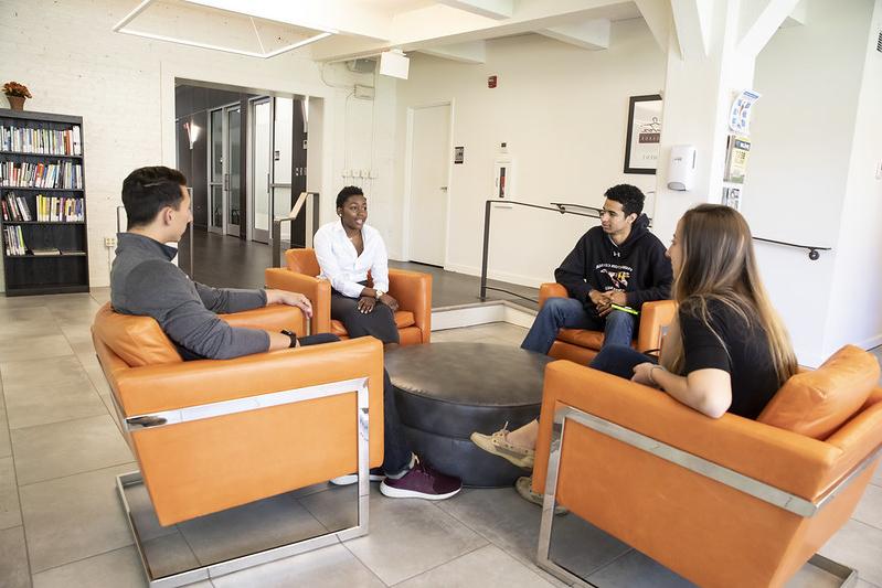 three students and a career counselor sit in lobby of career center smiling in orange chairs